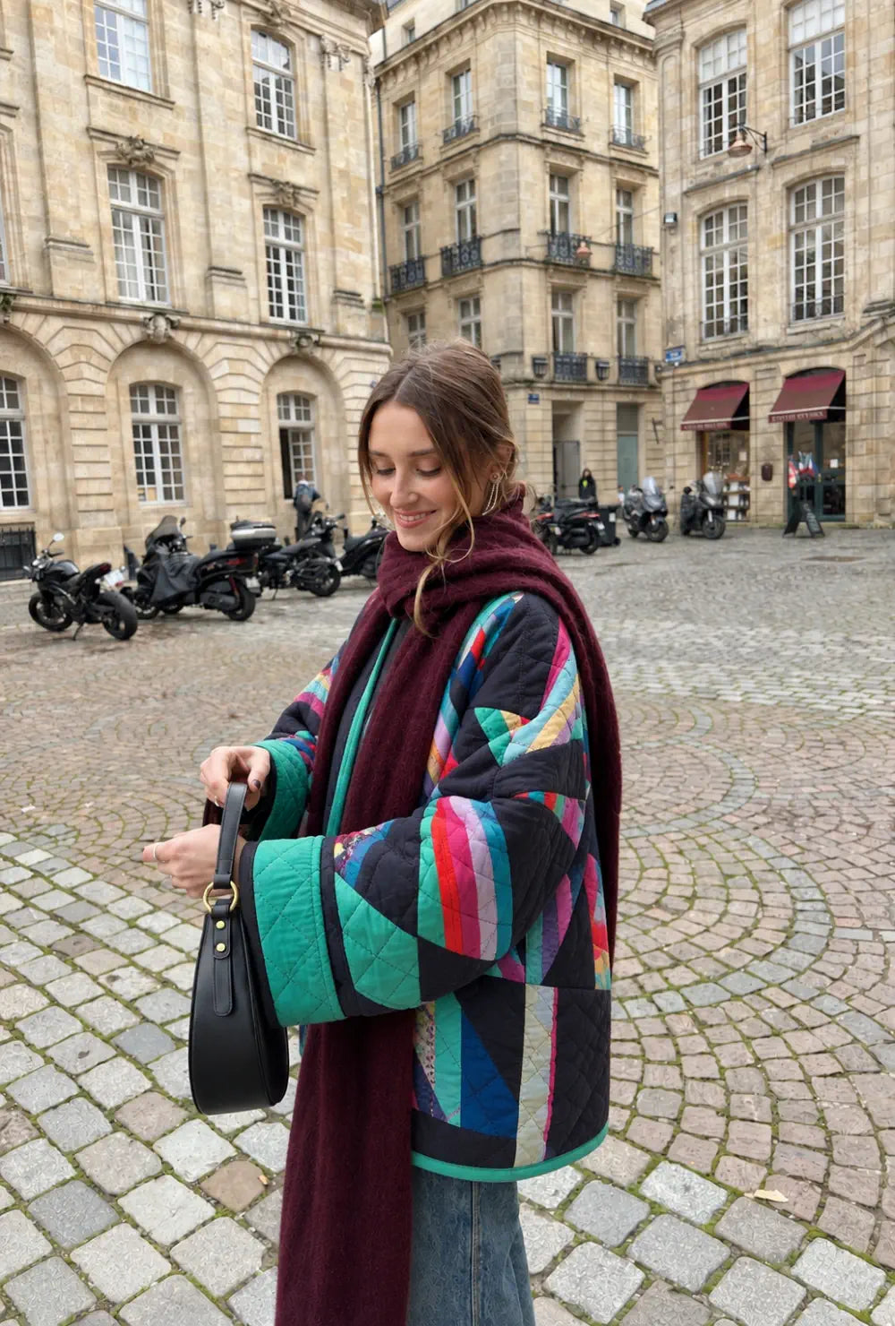 Blazer kimono matelassé femme multicolore style années 80 porté avec une écharpe bordeaux sur une place pavée