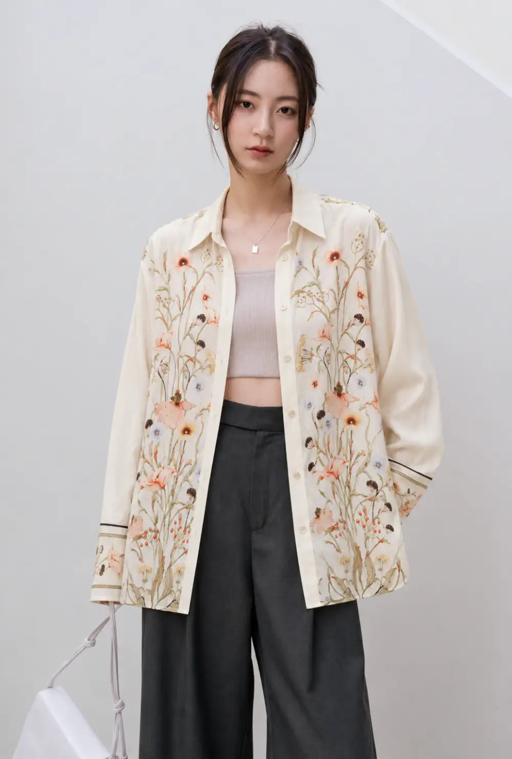 Chemise kimono femme beige courte à motif fleuri portée ouverte sur un top et un pantalon gris devant un mur blanc