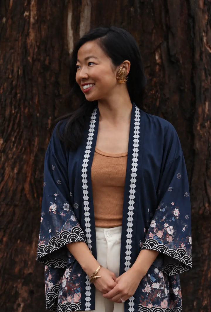 Kimono japonais femme bleu à motifs cerisiers et lanternes porté ouvert sur un débardeur camel devant un arbre