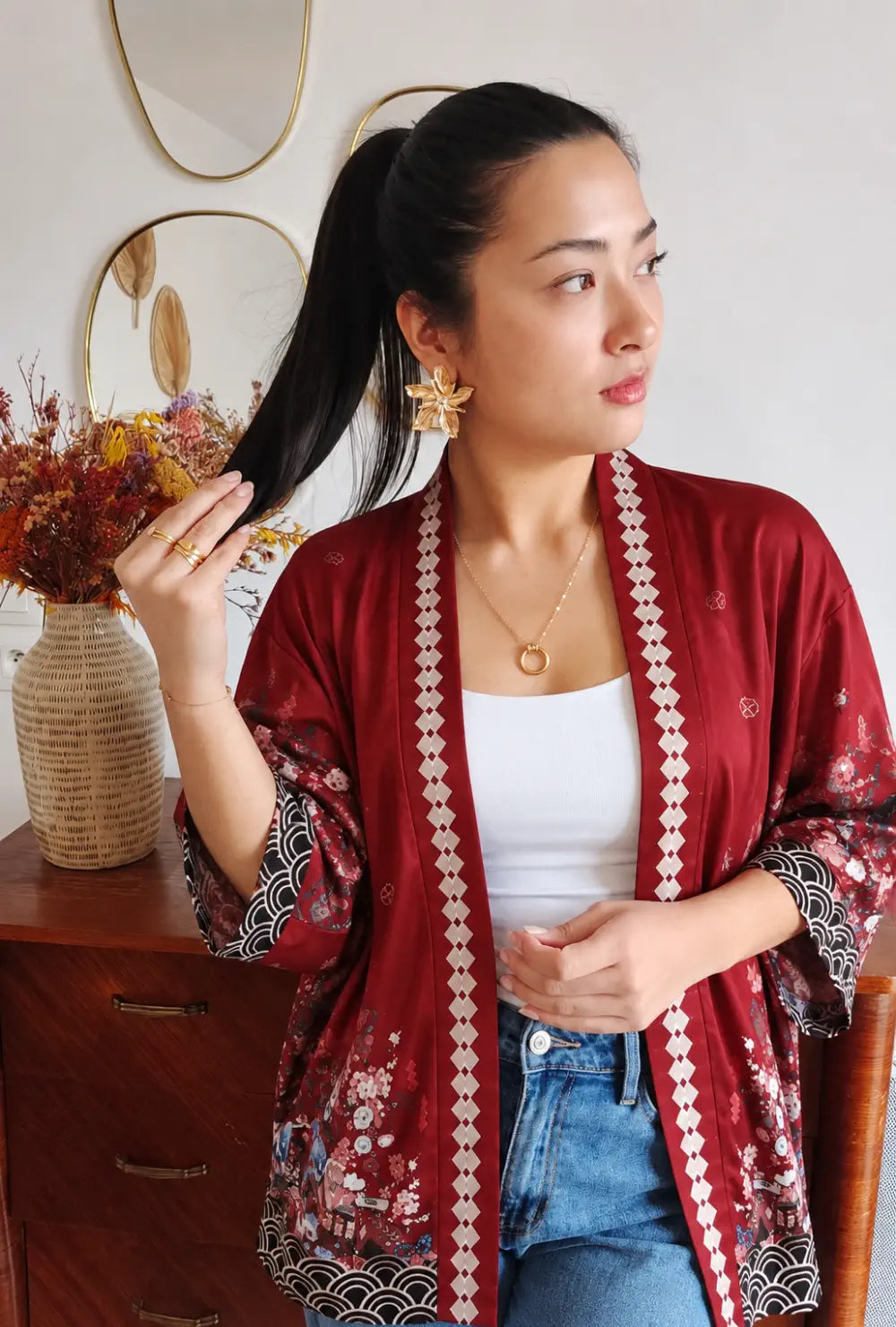 Kimono japonais femme rouge à motifs cerisiers et lanternes porté sur un top blanc et un jean dans un salon
