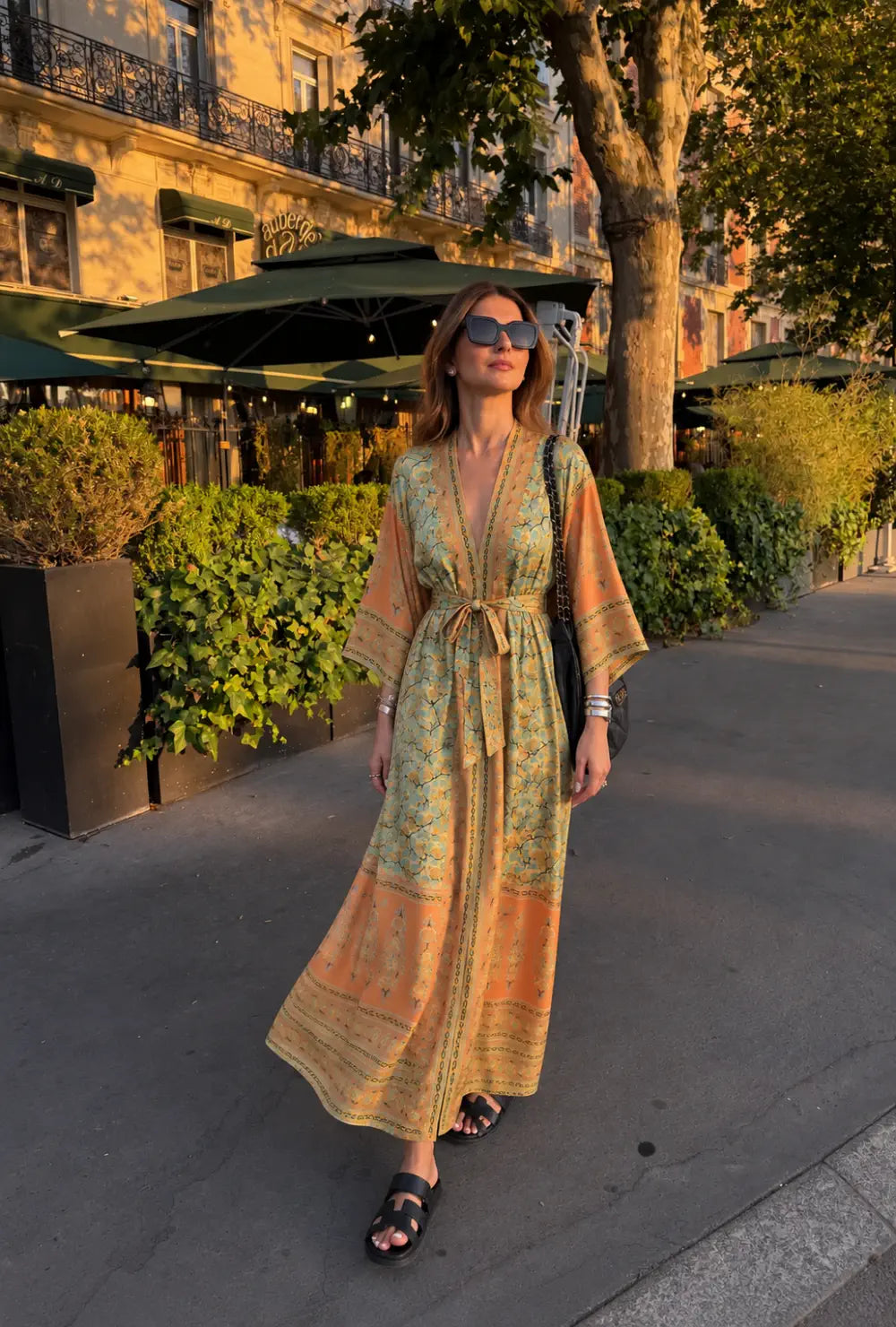 Kimono long femme orange et vert fleuri porté ceinturé avec des sandales noires en ville au coucher du soleil