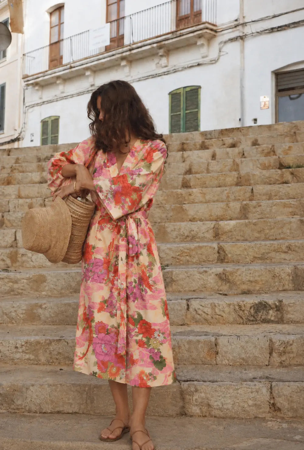 Kimono long femme rose pastel fleuri porté ceinturé avec un chapeau de paille sur des escaliers en pierre