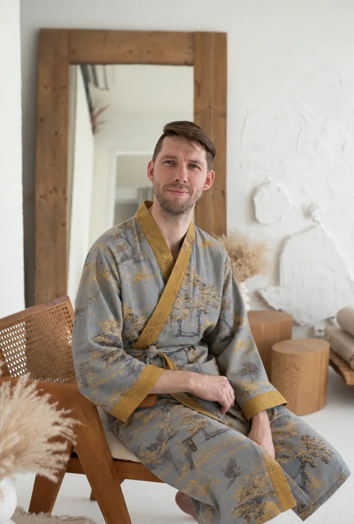 Peignoir japonais homme gris en coton à col V porté ceinturé, assis sur une chaise dans un intérieur blanc