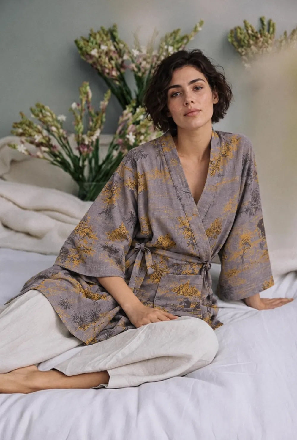 peignoir kimono gris porté assise sur un lit avec un pantalon crème