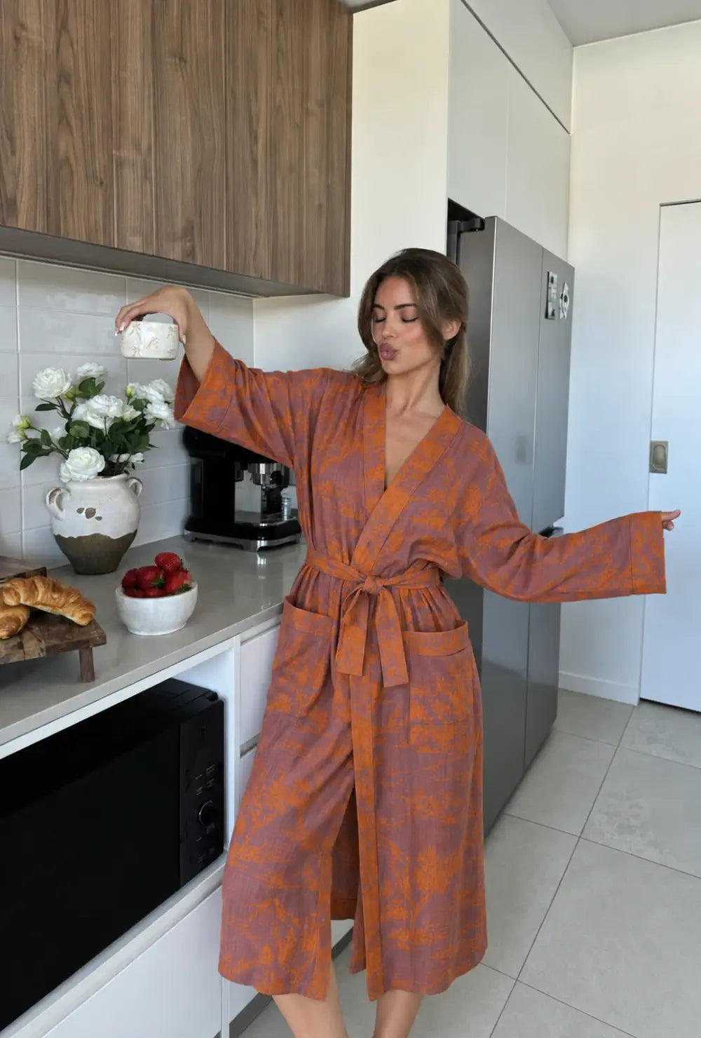 Peignoir kimono femme orange en coton à col V porté ceinturé bras ouverts dans une cuisine