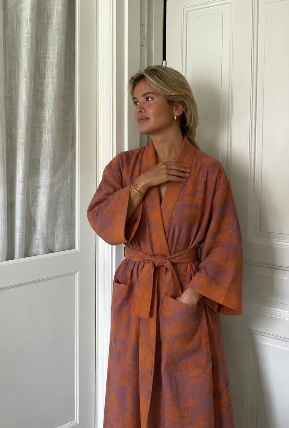 Peignoir kimono femme orange en coton à col V porté ceinturé main dans la poche devant une porte blanche
