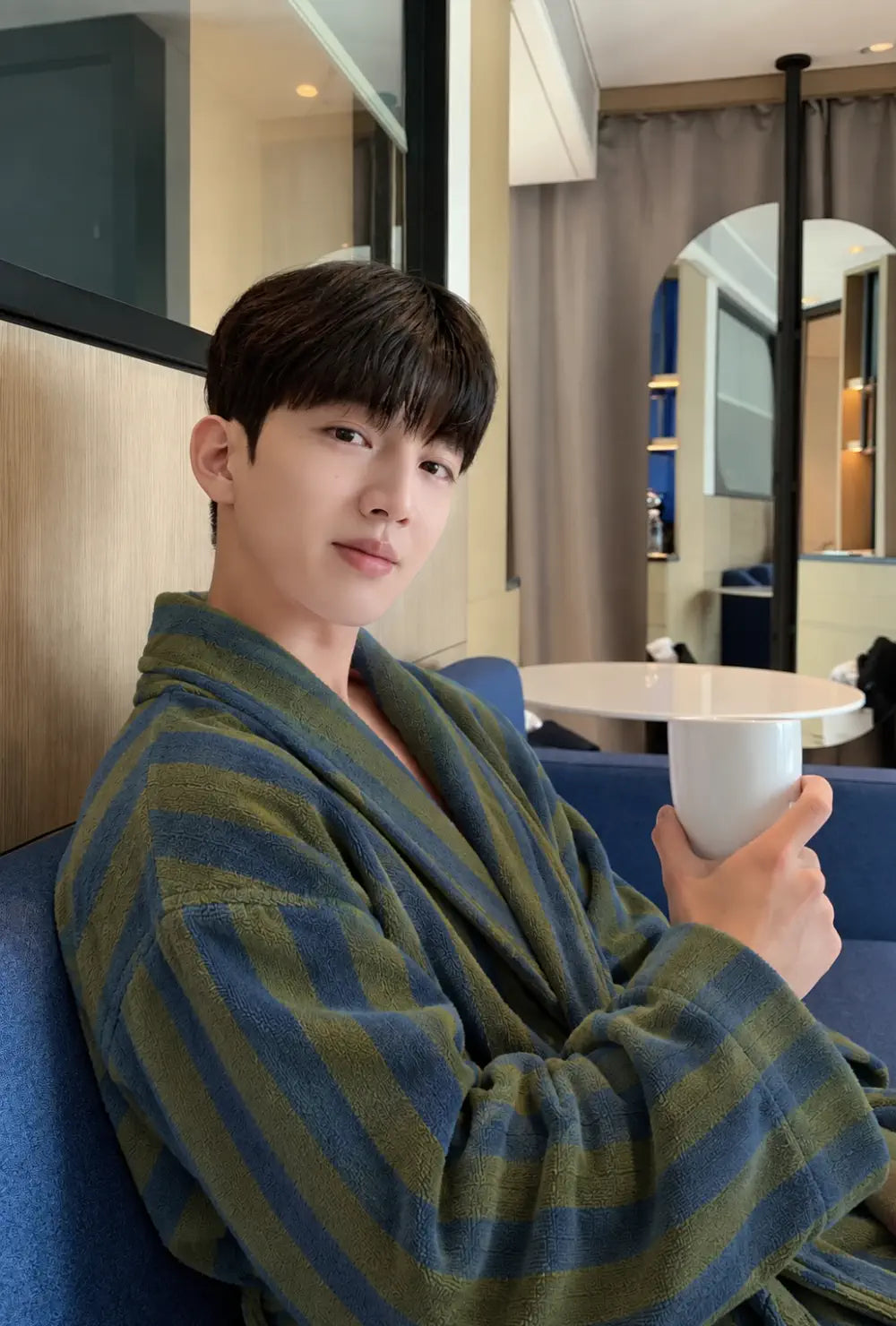Peignoir kimono homme vert en polaire chaude porté une tasse à la main, assis sur une banquette bleue
