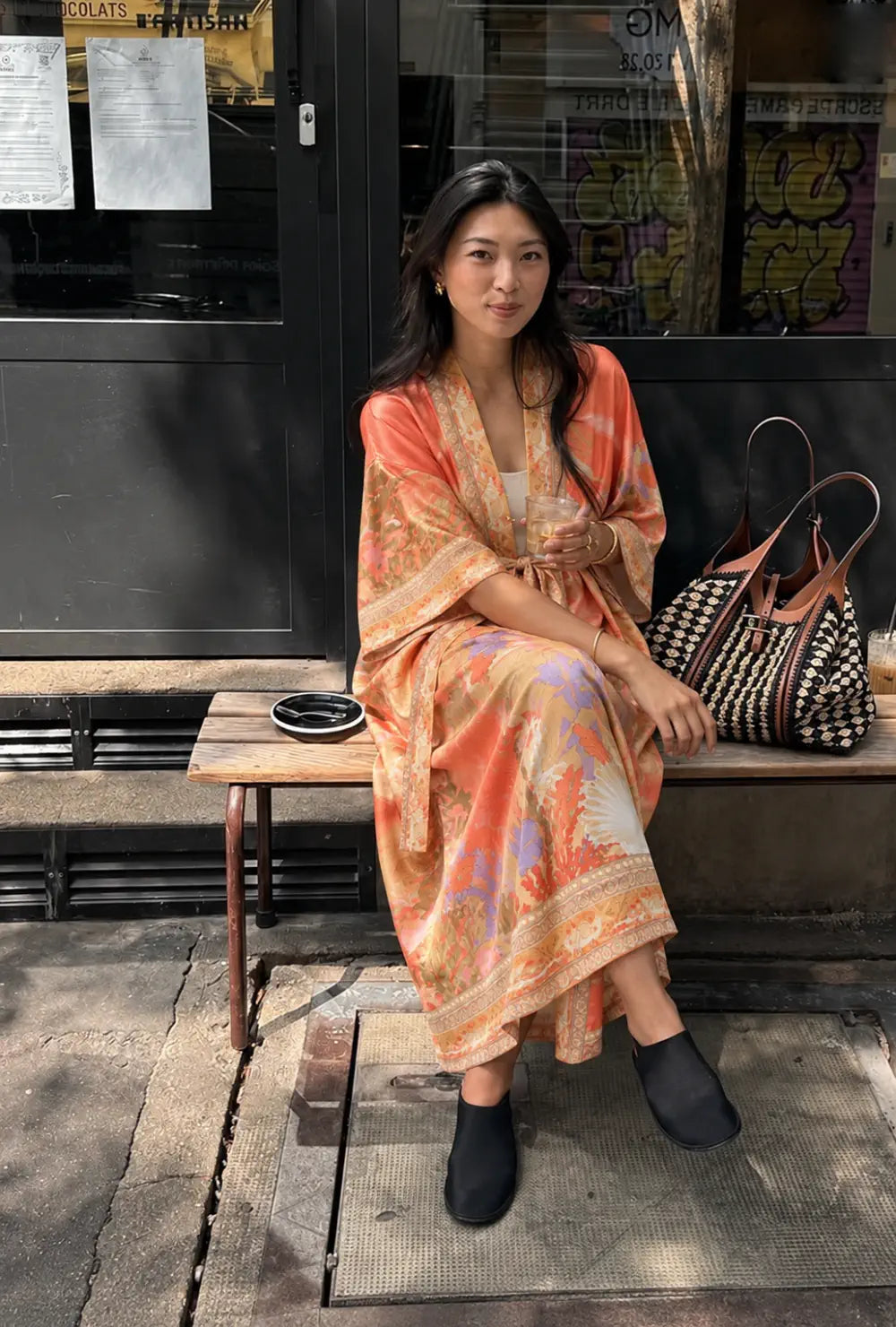Robe japonaise femme orange fleurie portée sur un top blanc assise sur un banc devant une boutique