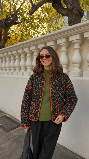 Veste kimono femme noire matelassée à fleurs portée ouverte sur un pull vert et un pantalon noir en ville