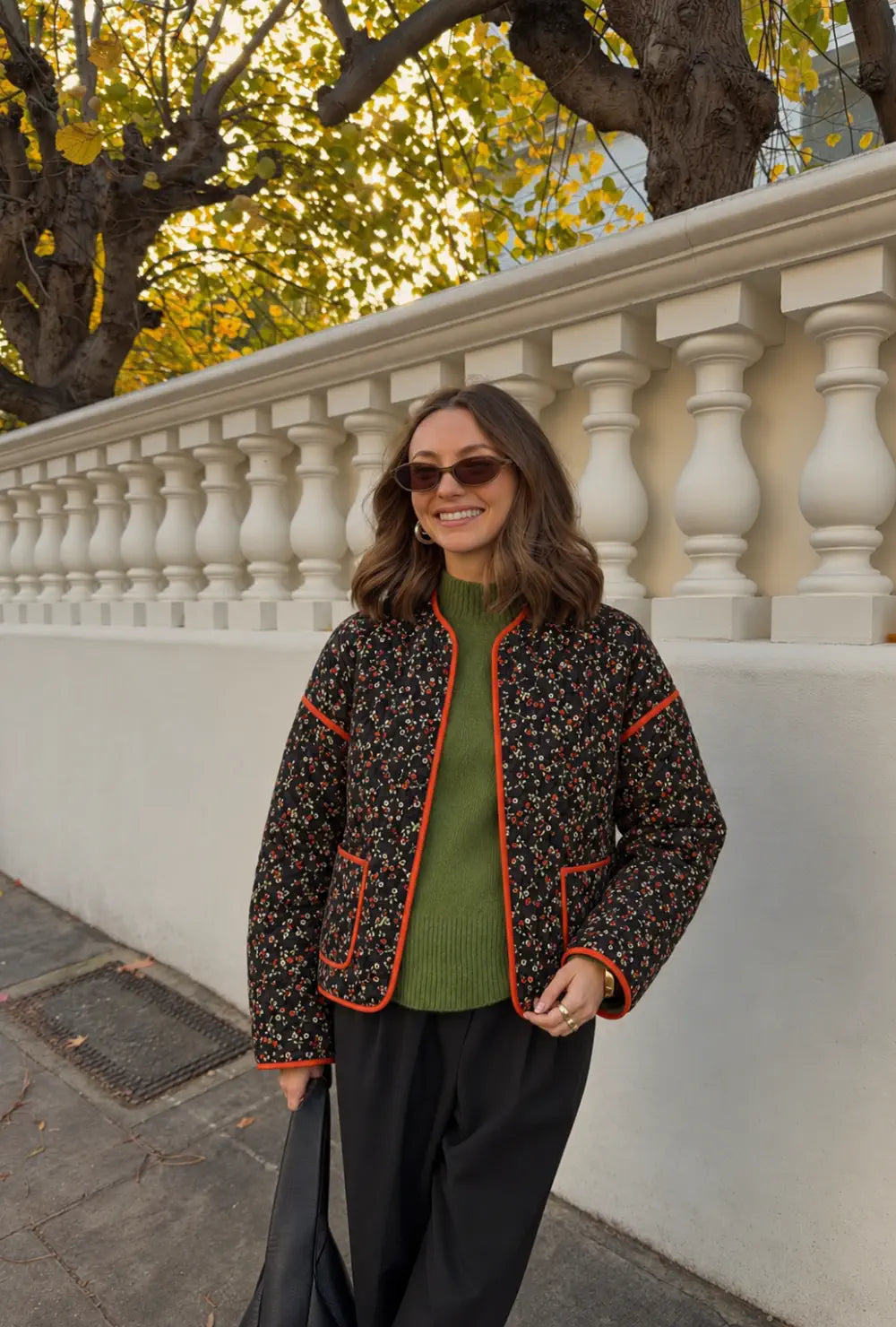 Veste kimono femme noire matelassée à fleurs portée ouverte sur un pull vert et un pantalon noir en ville