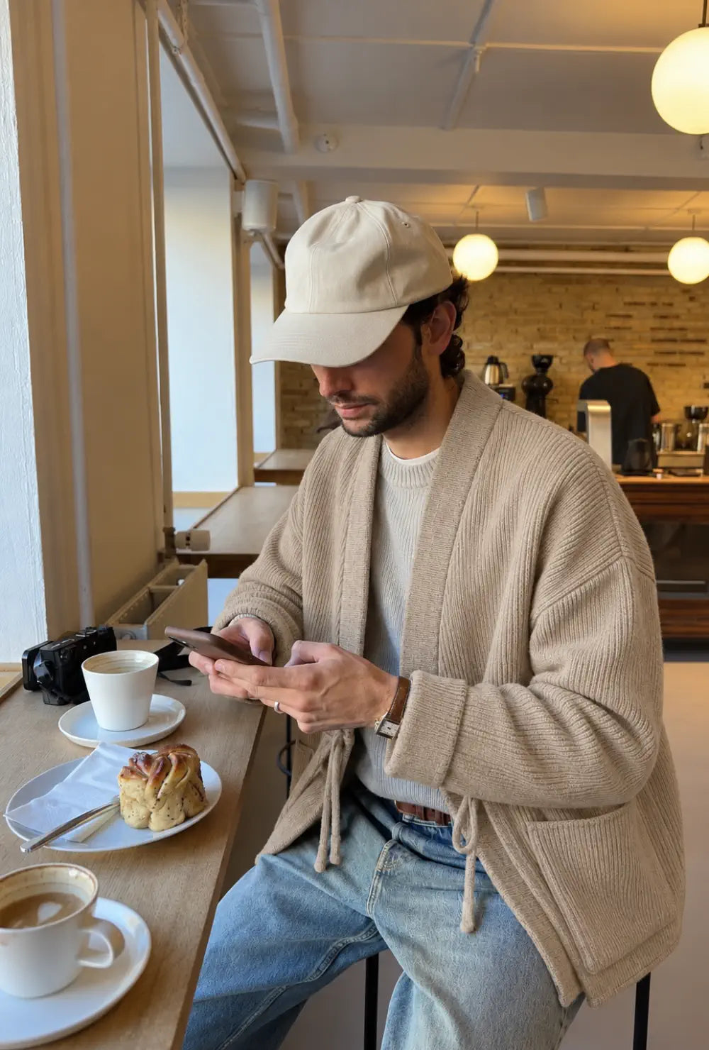 Veste kimono homme beige style cardigan portée ouverte sur un pull clair et un jean dans un café